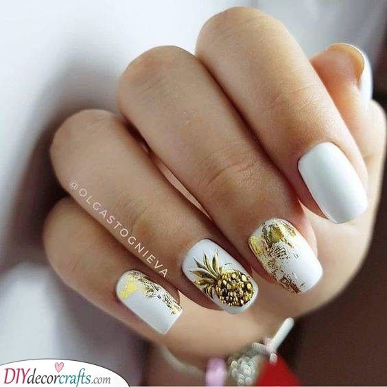 A gold pineapple on an accent nail on white base polish
